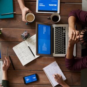 Group of coworkers discussing business strategies with laptops and tablets in a modern office setting.