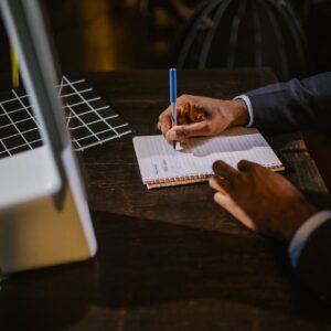 A businessman in a suit writing notes on a notebook at a desk, suggesting a professional office environment.