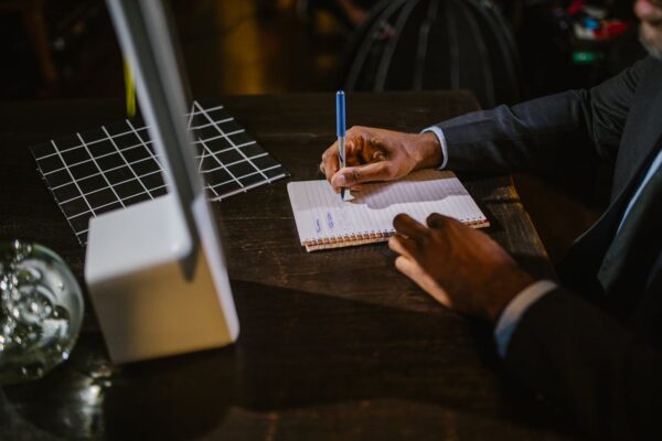 pexels-photo-6517328 A businessman in a suit writing notes on a notebook at a desk, suggesting a professional office environment.