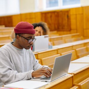 Students focus on laptops in a spacious university lecture hall, learning and working digitally.